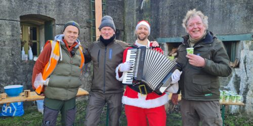 Lofzanger Joost met zijn accordeon op de foto verkleed als Kerstman. Naast hem staan 3 boswachters van Natuurmonumenten.