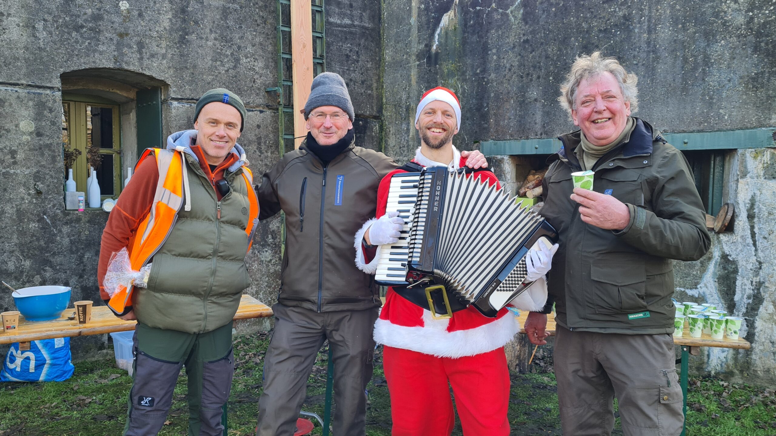 Lofzanger Joost met zijn accordeon op de foto verkleed als Kerstman. Naast hem staan 3 boswachters van Natuurmonumenten.