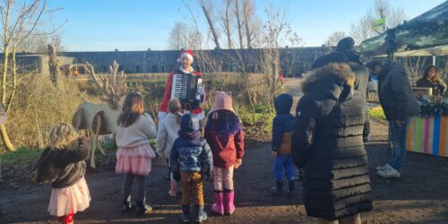 De Kerstman speelt liedjes voor jong en oud. Hier vermaakt hij een groepje kinderen met live kerstmuziek op een event van Natuurmonumenten.